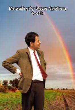 A businessman in a rural field under a rainbow, waiting for a call that will never come. Absurdist hope meets rural emptiness.