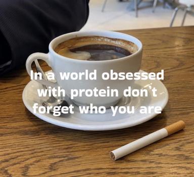 Coffee mug with cigarette on wooden café table; existential text overlay on wellness culture.