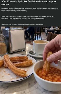 A dark text block above a photo of churros on a white plate with a blue rim, beside a cup of coffee and a napkin dispenser. A hand dips a churro into a bowl of baked beans in tomato sauce, captioned as a supposed improvement on Spanish churros.