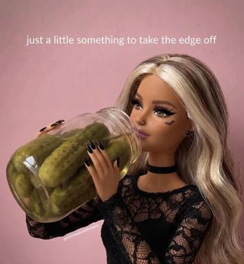 A blonde, fashion-doll-style figure with a nose ring, bat face tattoo and black lace top hugs a large glass jar of dill pickles against a flat pink backdrop. The caption across the top reads "just a little something to take the edge off", a joke about the pickles as a stress reliever.