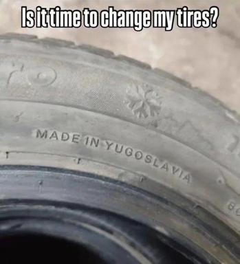 A close-up photo of a worn winter tire sidewall with a snowflake (M+S) symbol and the embossed words "MADE IN YUGOSLAVIA". The top caption asks, "Is it time to change my tires?" The joke is that the tire is so old it comes from a country that no longer exists.