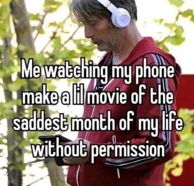 A person sitting outdoors with headphones, looking at their phone to film a "lil movie," capturing an intimate, awkward moment.